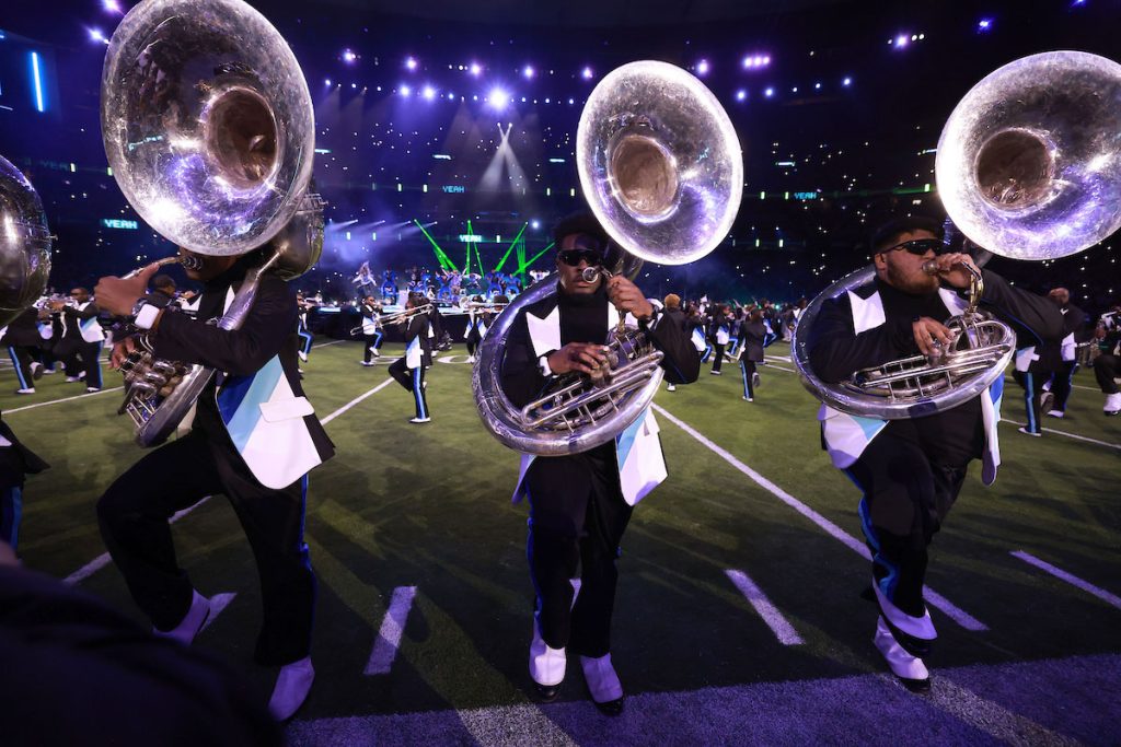 A line of tuba players on a lit football field at night