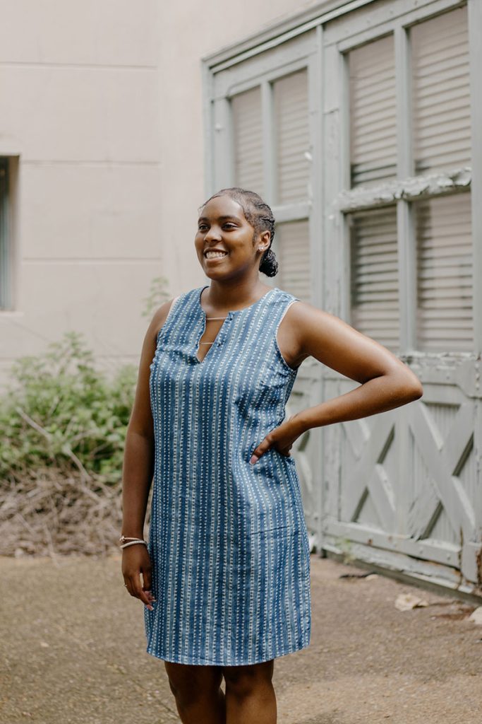 A teen stands in a courtyard wearing a blue striped top smiles and looks to the distance