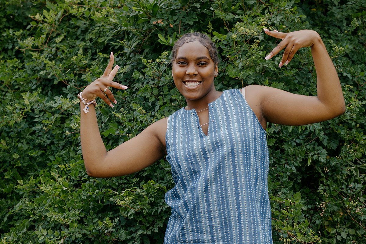 A teen in a blue striped top smiles with hands raised