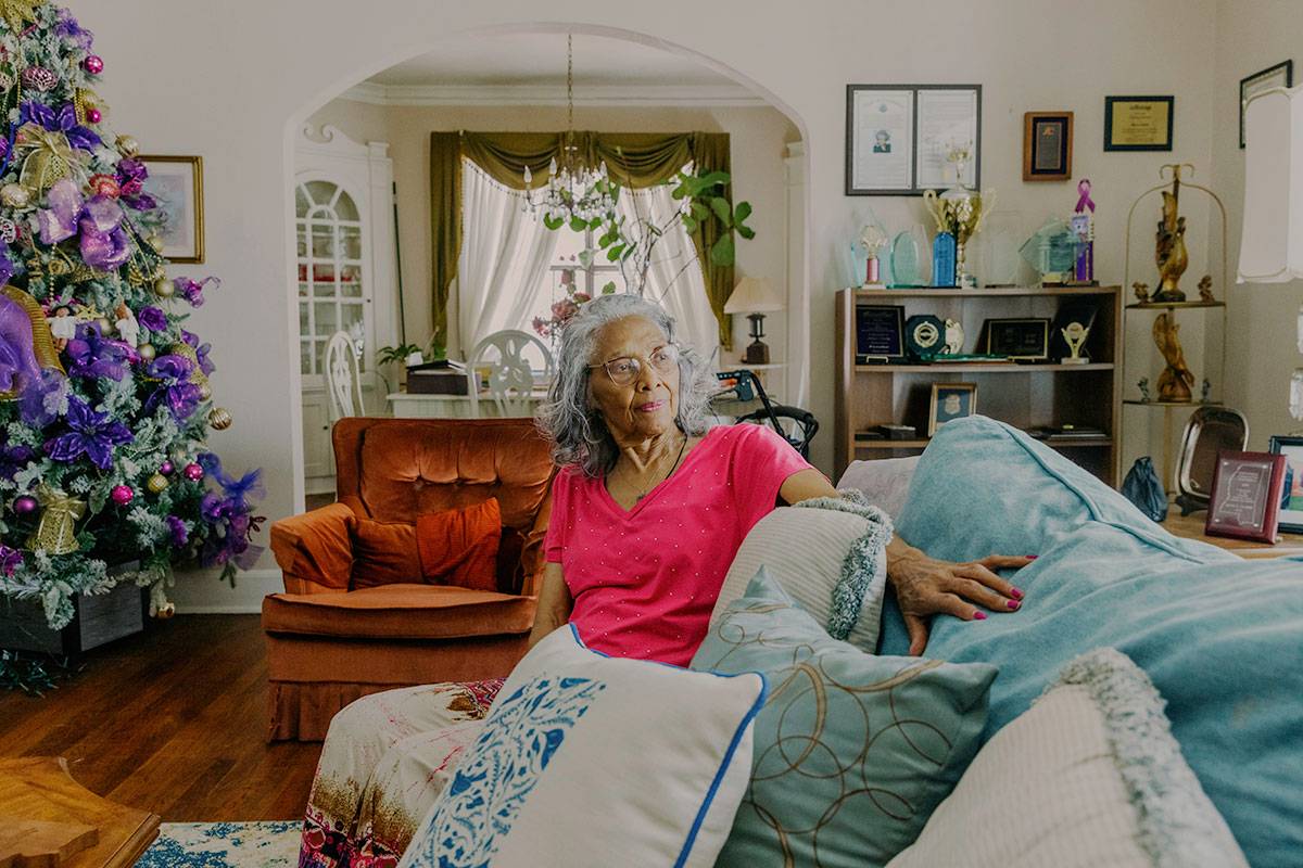 A woman in a pink top sits on a couch in a well lit living room.