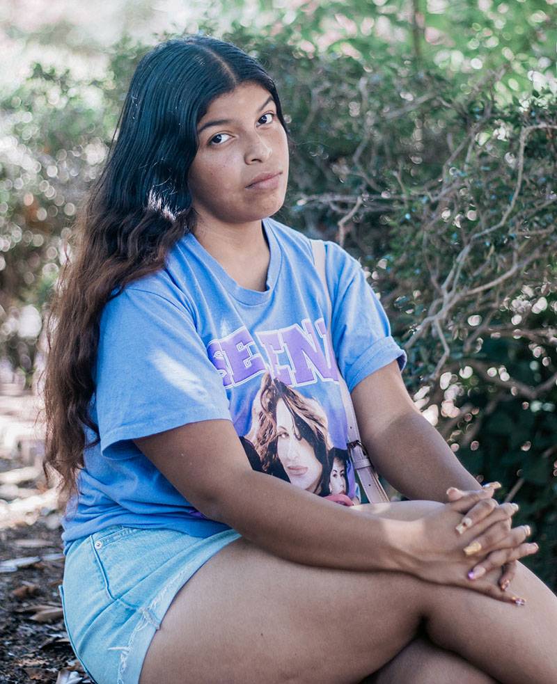 A teen in a blue outfit sits outside