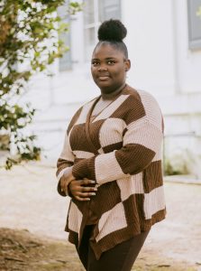 A teen in a brown checkered sweater poses outside