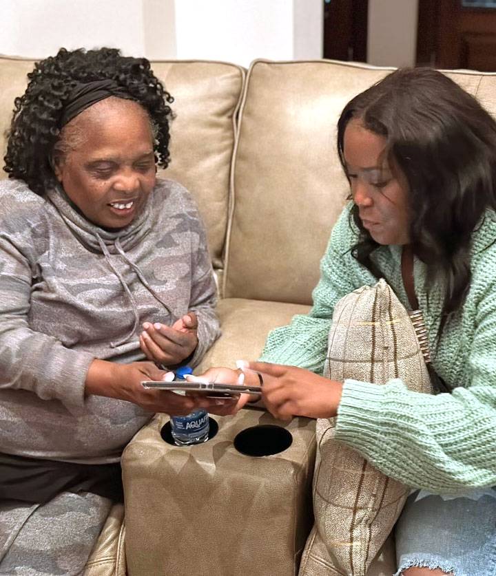 A teen and her grandmother sit on a couch and look together at a phone