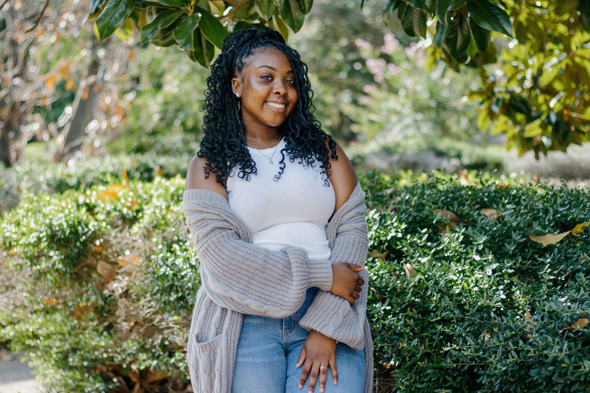 A teen in a grey sweater poses outside under a magnolia tree