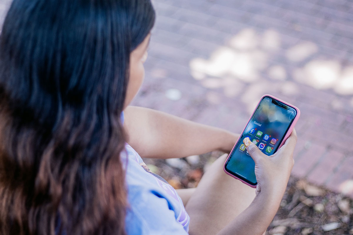 An over the shoulder view of a teen looking at a cell phone screen filled with social media apps