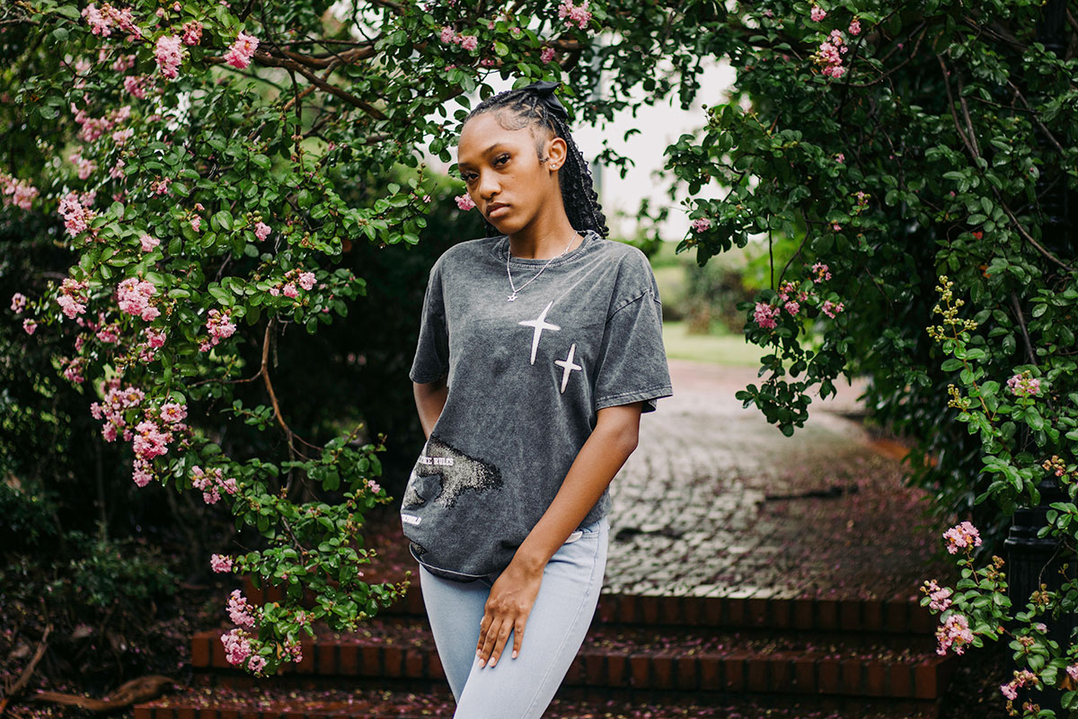 A teen poses outside under a pink flowering tree