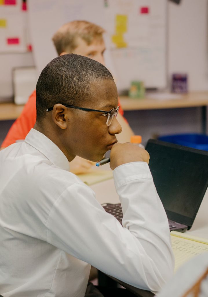 A teen in a dress shirt sits at a laptop, looking to the right with focus