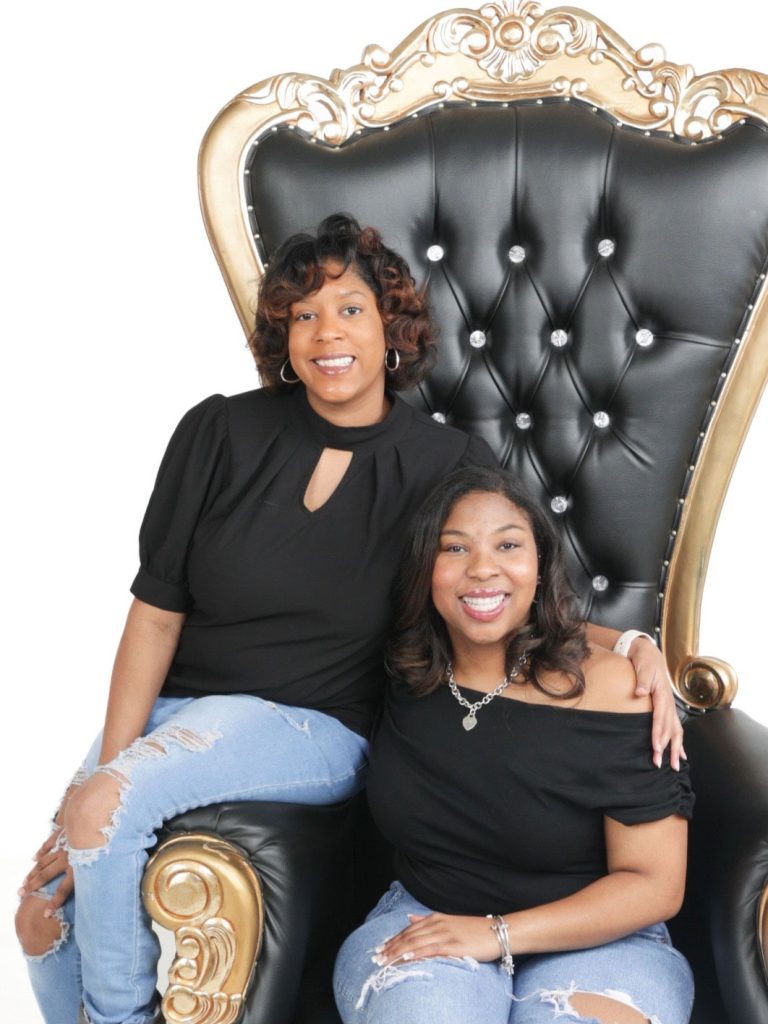 Two teens in matching outfits of black tops and bluejeans pose on a throne-like black and gold chair