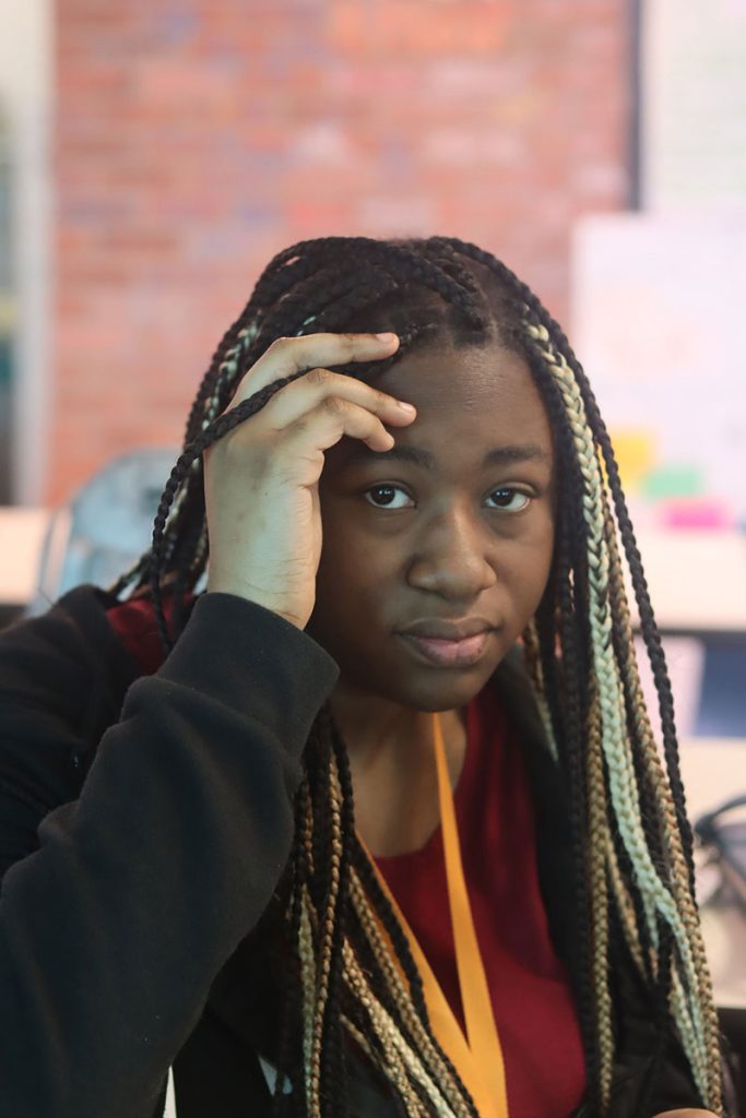 A teen holds a hand on her head and looks at the viewer