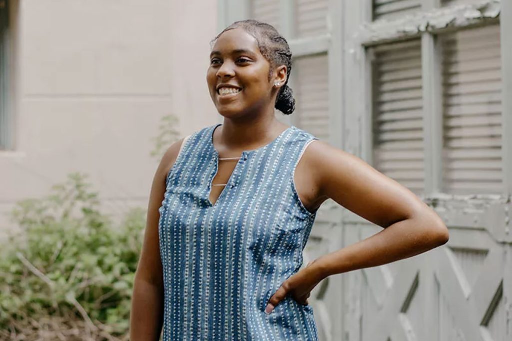 A teen stands in a courtyard wearing a blue striped top smiles and looks to the distance