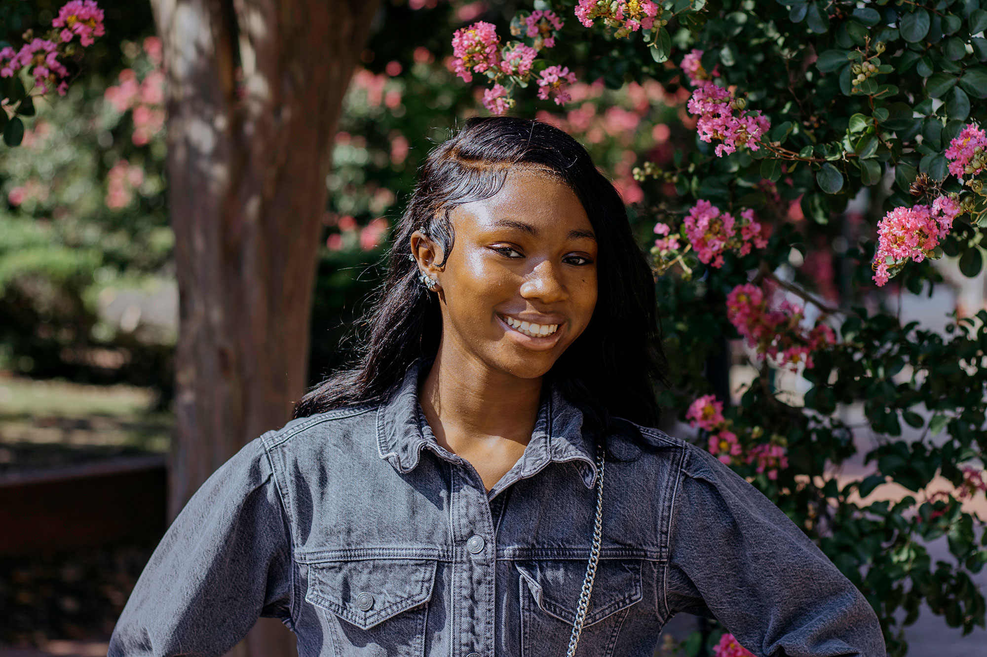 A teen stands outside in front of a pink flowering tree